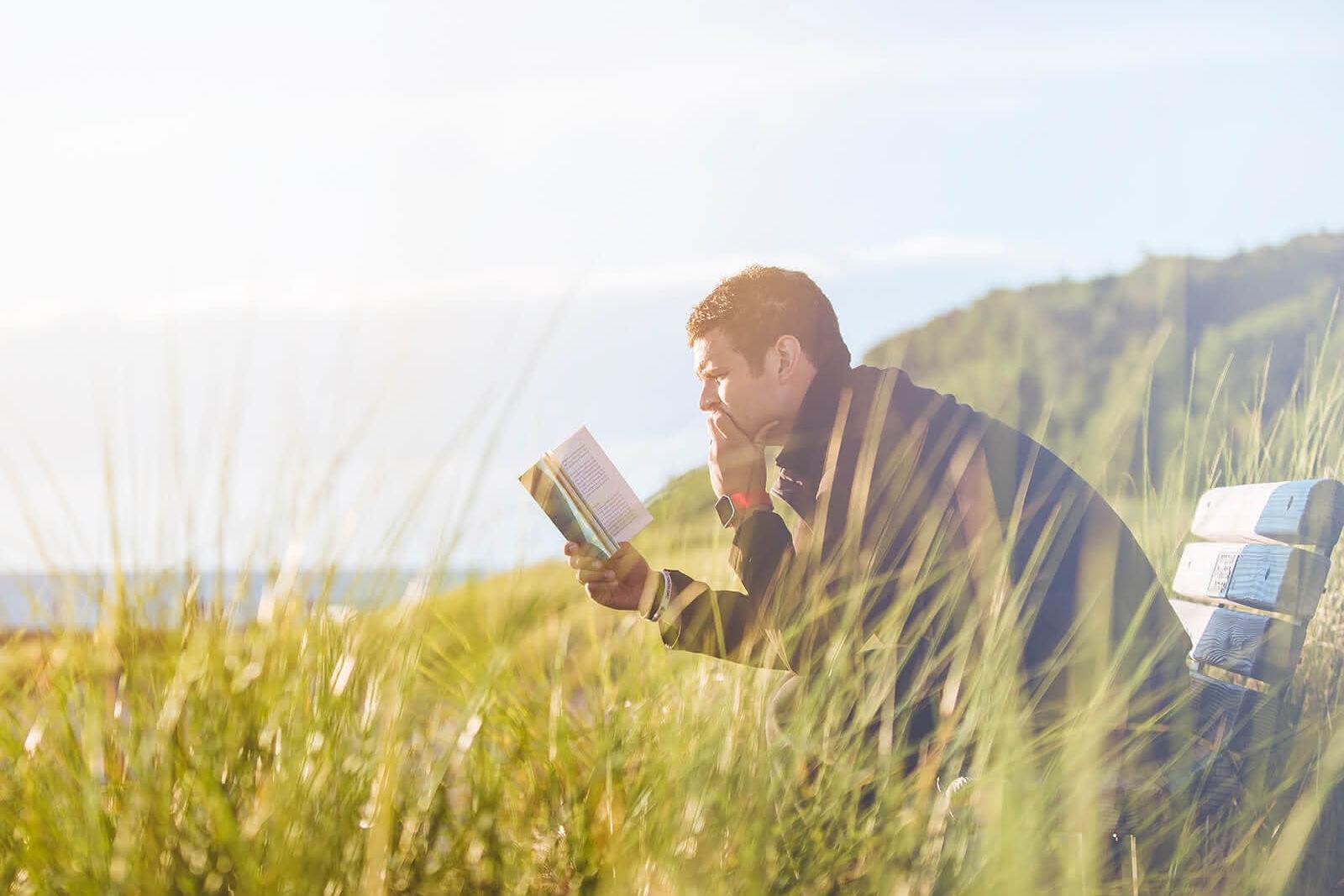 Mann mit Buch auf einer Bank in einer Wiese