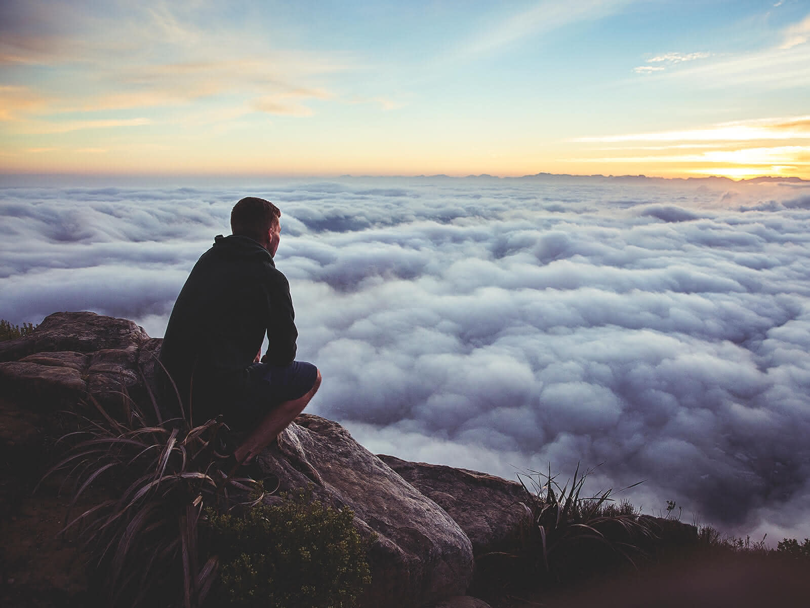 Mann sitzt auf einem Felsen über den Wolken